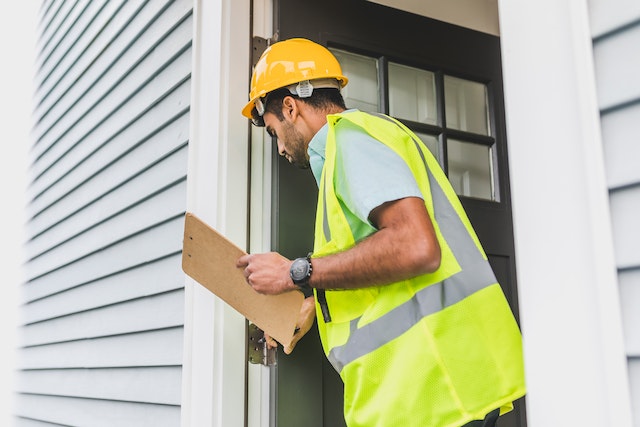 a contractor in a yellow vest inspects the front door of a rental property to ensure it adheres to building codes